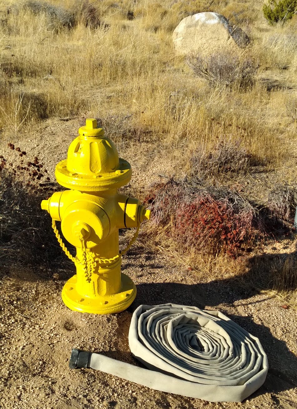 A yellow fire hydrant with a coiled hose beside it, located in a dry grassy area.