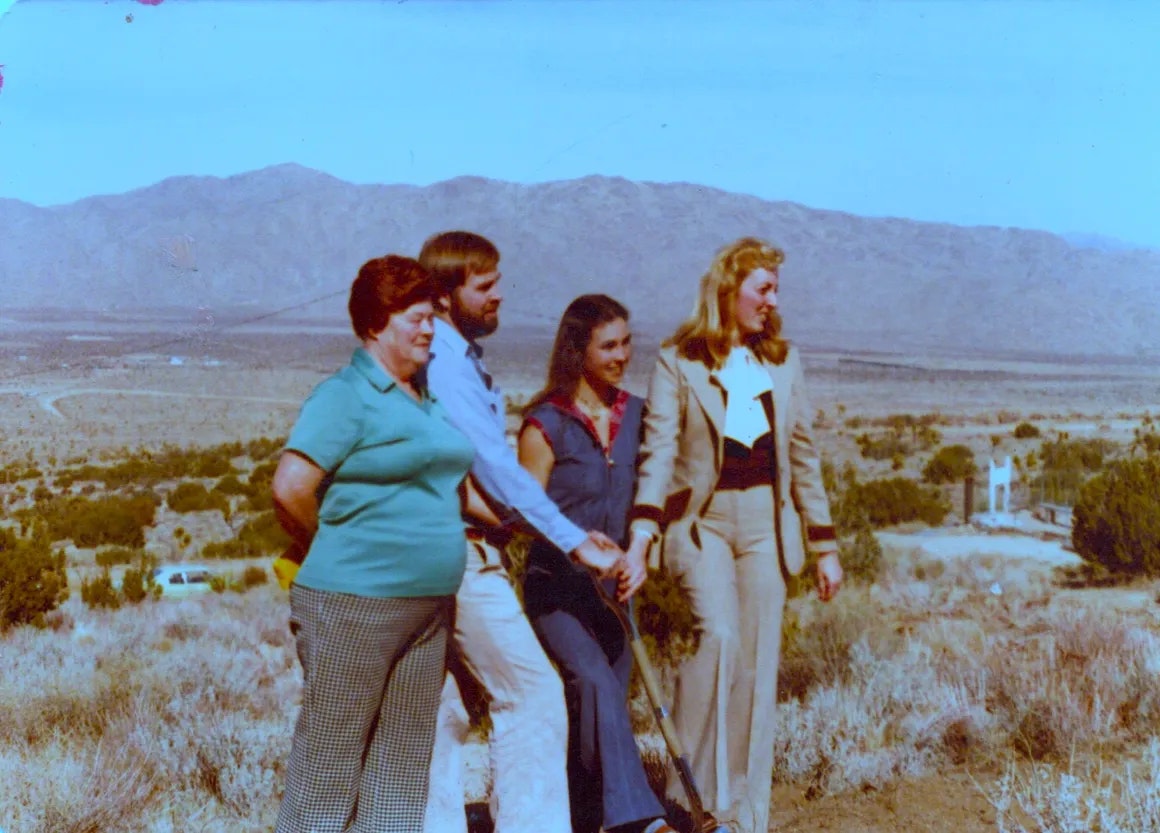 Four people in vintage attire standing in a desert landscape.