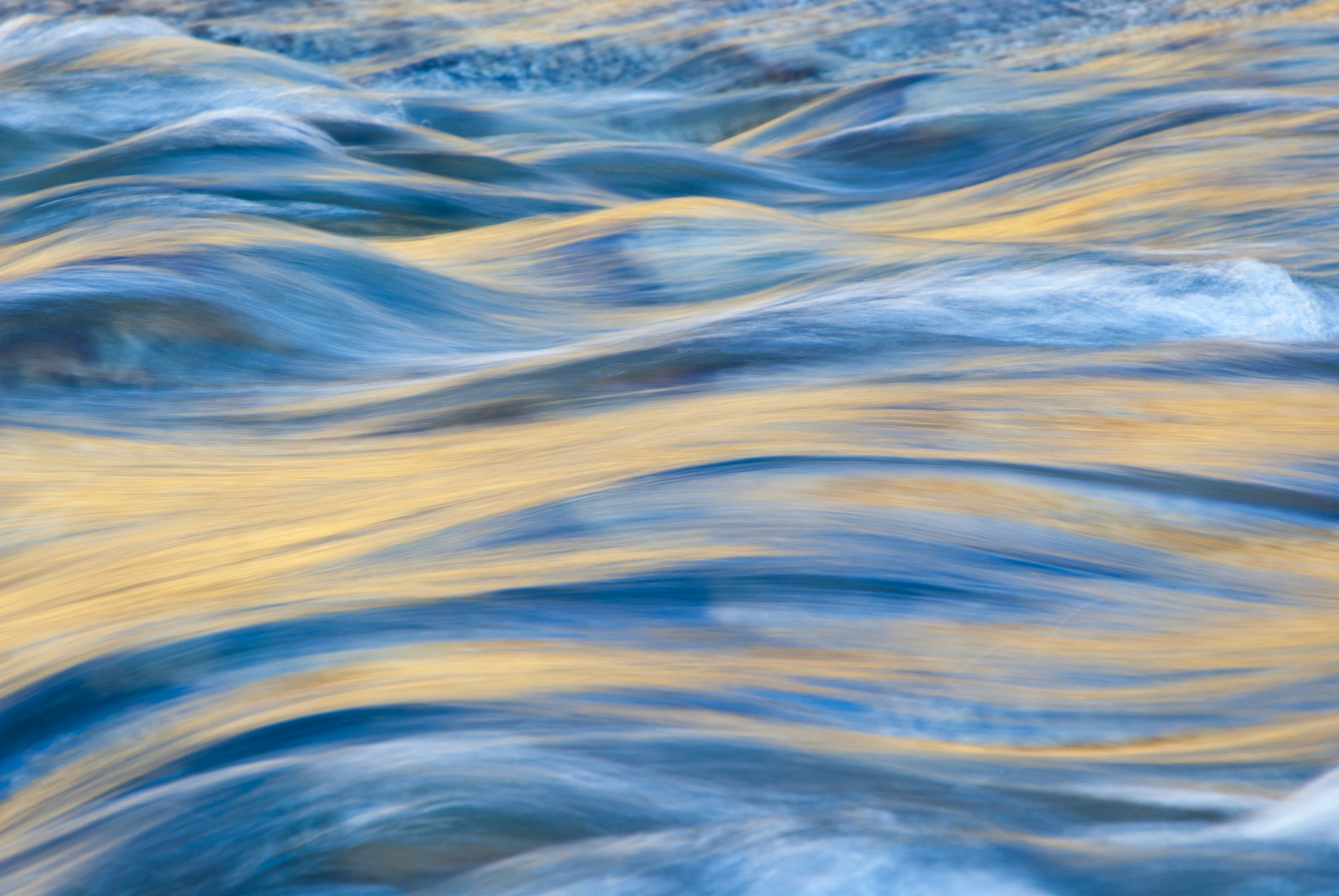 Rippling water with blue and golden hues, likely captured in motion for an abstract effect.