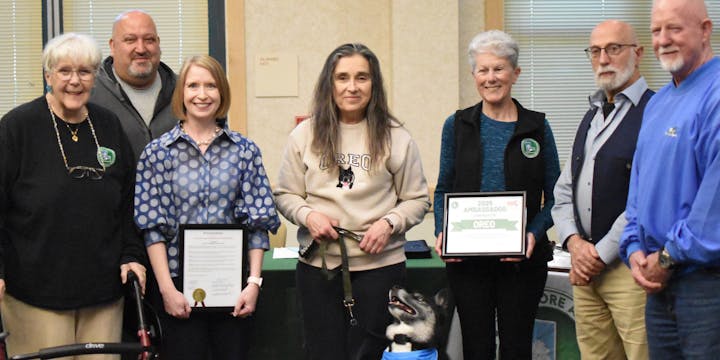 A group of people posing with a dog holding a certificate labeled "2023 Ambassadog" and a proclamation document.