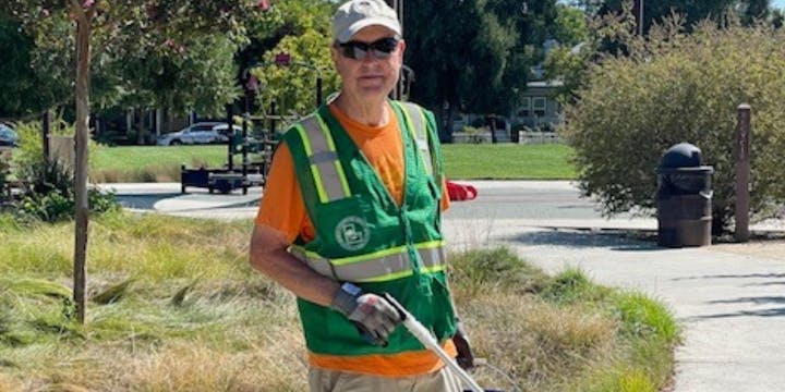 A person in a reflective vest with a grabber tool and a trash bag, likely doing community cleanup.