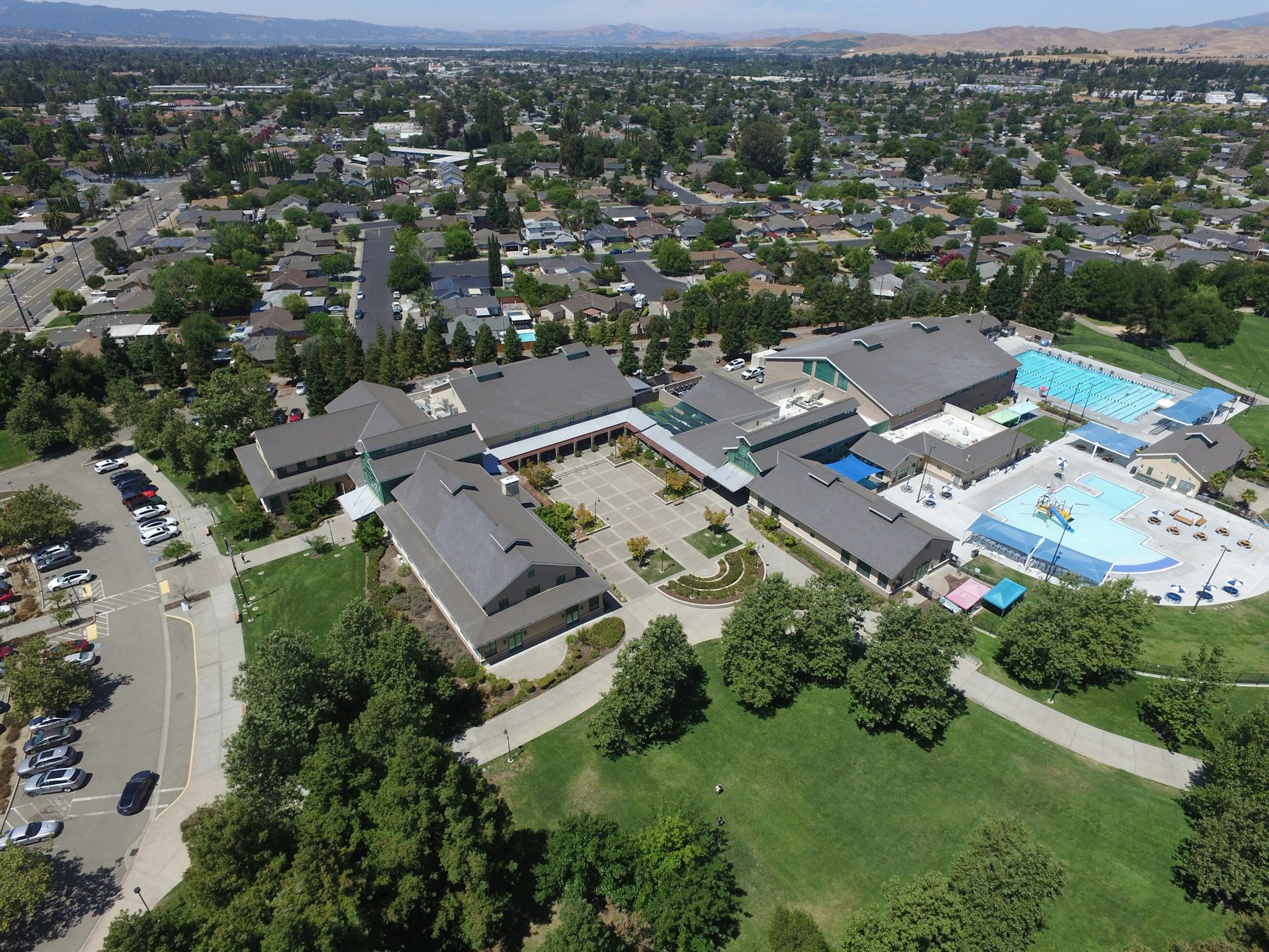 Aerial view of a community center with swimming pool, parking, and green spaces surrounded by a residential area.