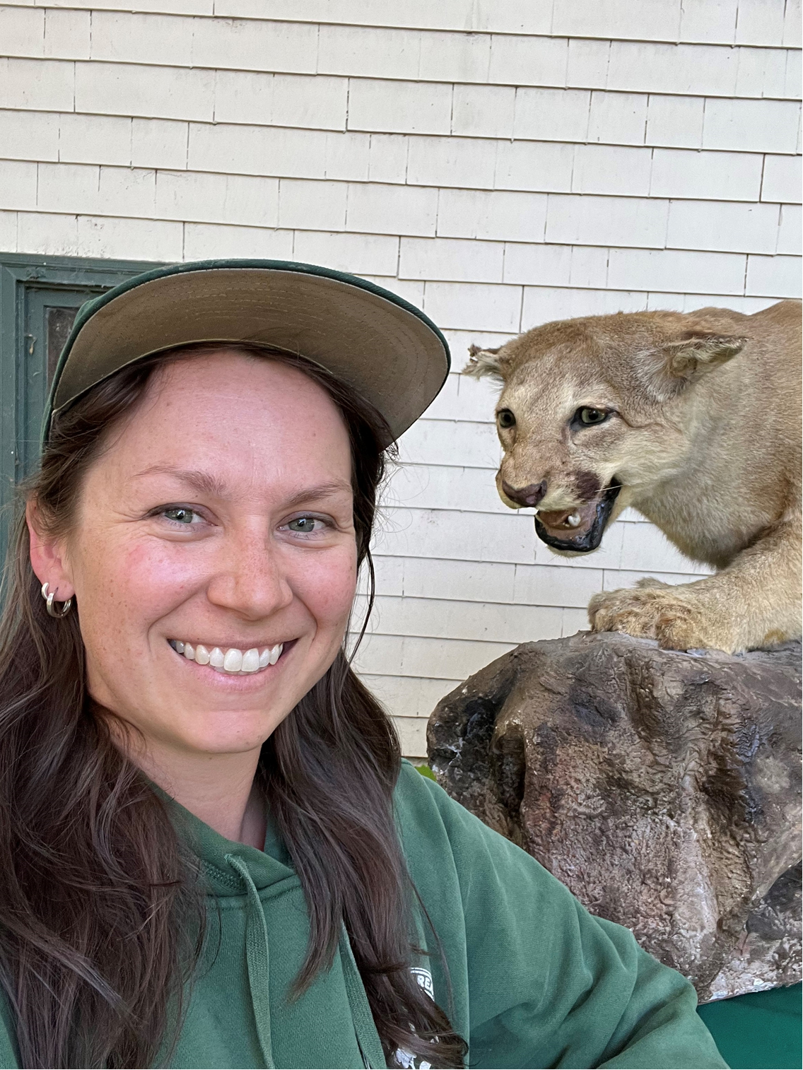 A woman taking a selfie with a mounted mountain lion in the background. #SelfieWithWildlife