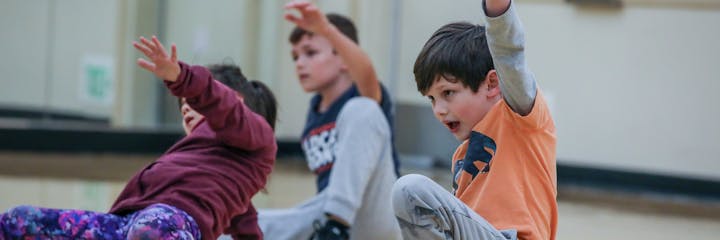 Three children are engaged in a movement activity, actively participating and expressing enthusiasm in a playful environment.