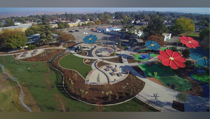 An aerial view of a colorful playground with large flower decorations, walking paths, benches, and landscaped gardens.