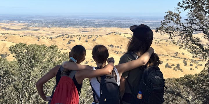Four people with backpacks enjoying a scenic overlook with dry hills and trees in the background.