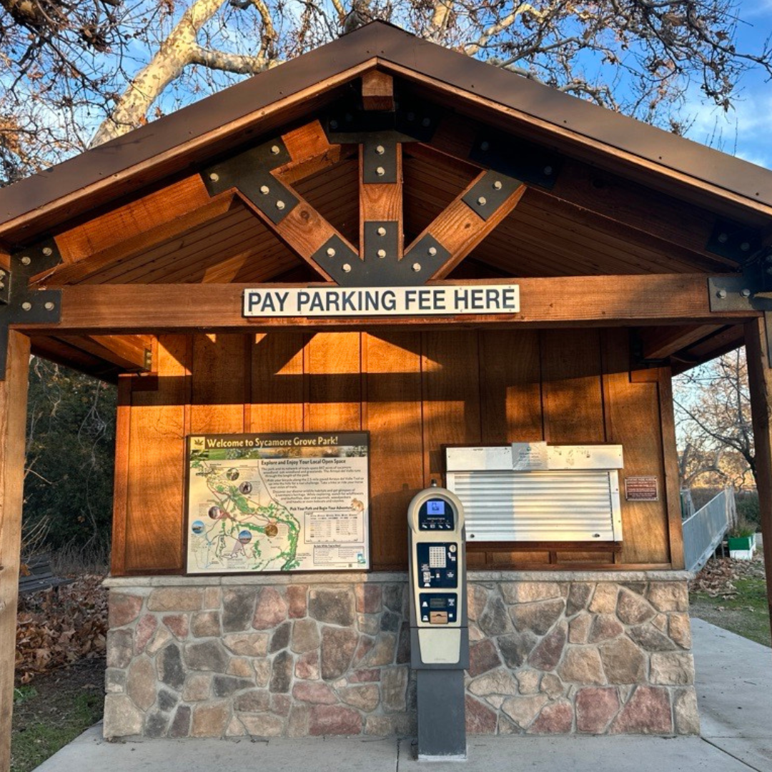 A wooden kiosk at Sycamore Grove Park with a sign for parking fees and an information map.