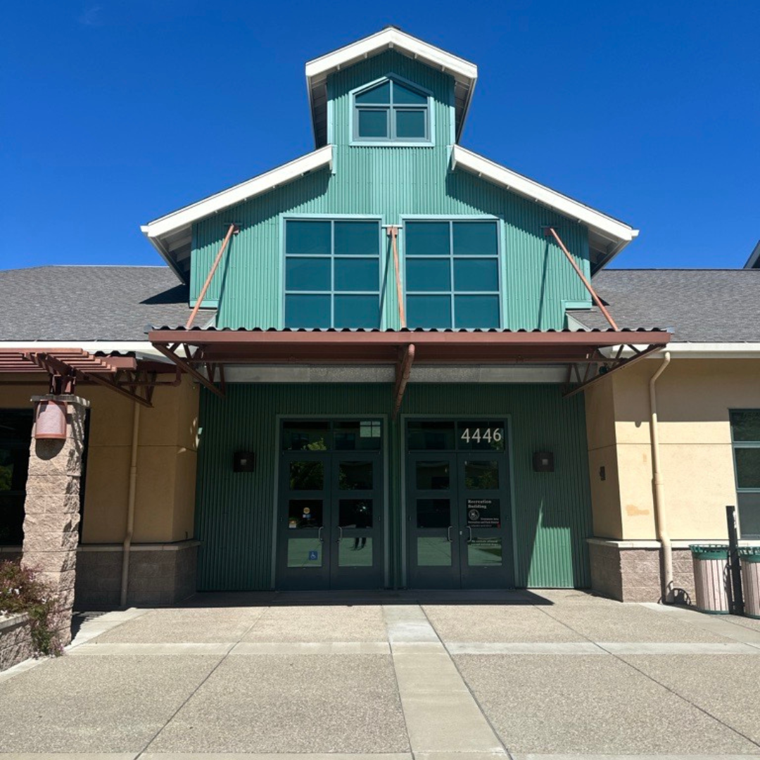 Building entrance with green facade and windows, numbered 4446, under a blue sky.