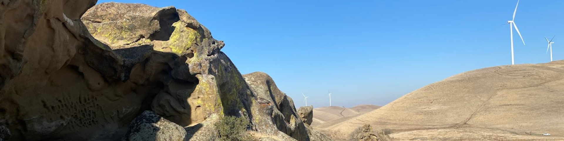 Desert landscape with eroded rocks and wind turbines under a clear blue sky.
