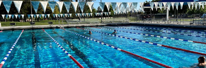 Outdoor swimming pool with lane dividers and a few swimmers.