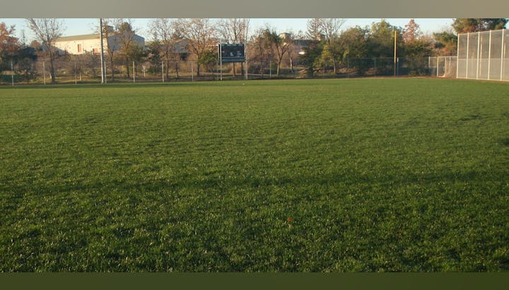 A baseball field with green grass, a score board, and a fence in the background.