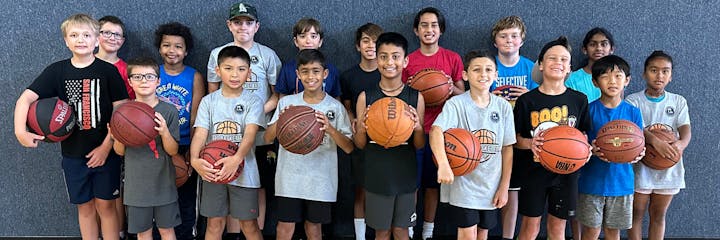 A diverse group of kids holds basketballs, posing together in a gym or sports facility.