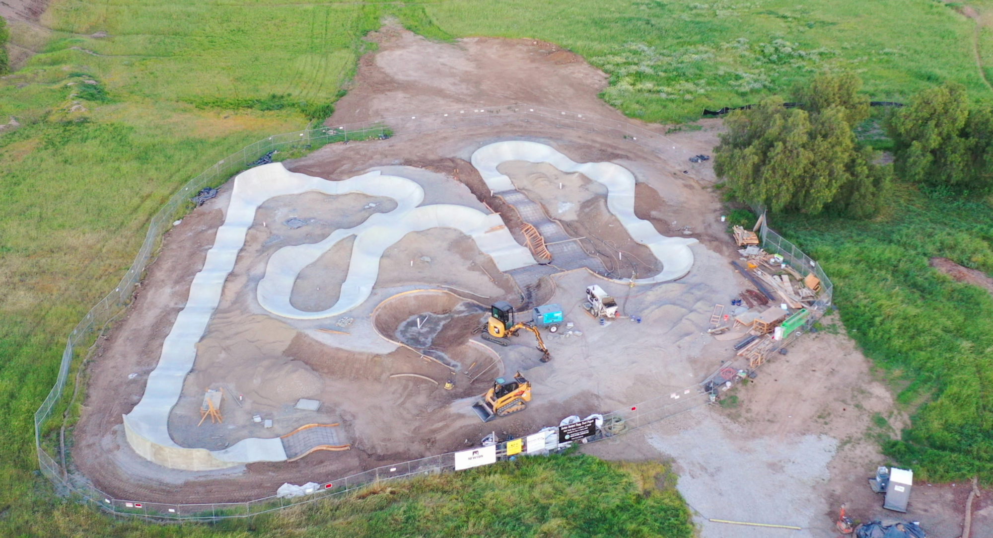 Aerial view of a construction site for a skatepark with curved concrete features and construction equipment nearby.