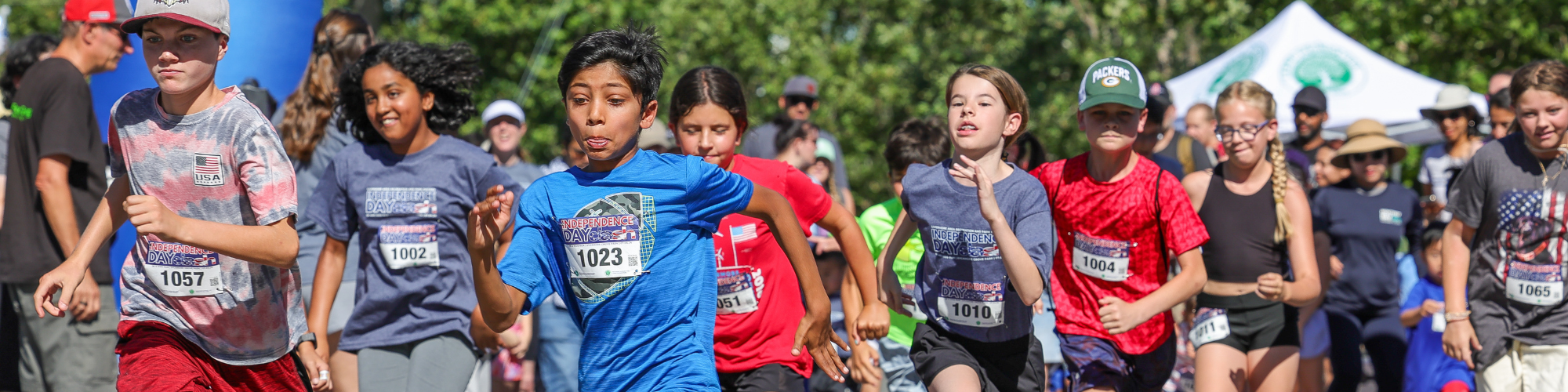 Kids are participating in a lively race, wearing numbered shirts and celebrating an event, likely related to Independence Day.