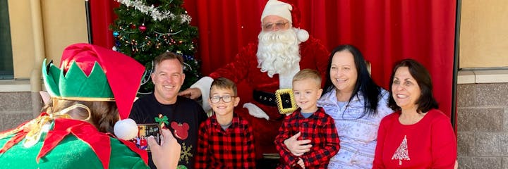A family poses with Santa Claus while an elf takes their photo.