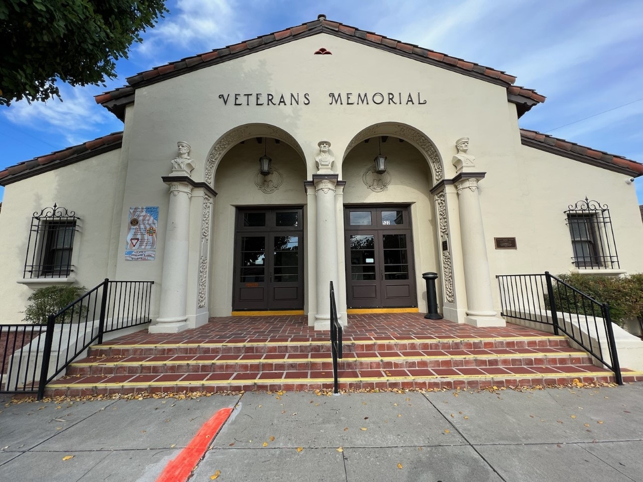 A beige building with "Veterans Memorial" on it, featuring steps, columns, and decorative elements.