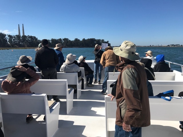 People wearing hats on a boat ride, enjoying the sunny weather with a waterfront view.