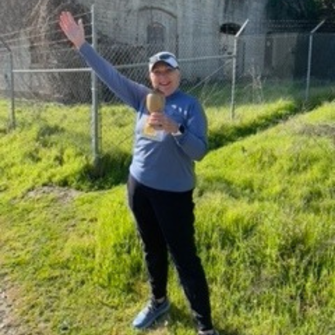 A person with a raised arm holding a trophy, outdoors, smiling.