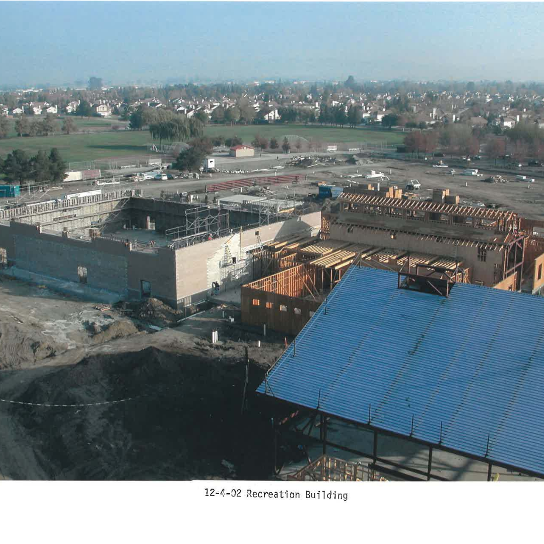 Construction site with a building under development, surrounded by open land and residential area.