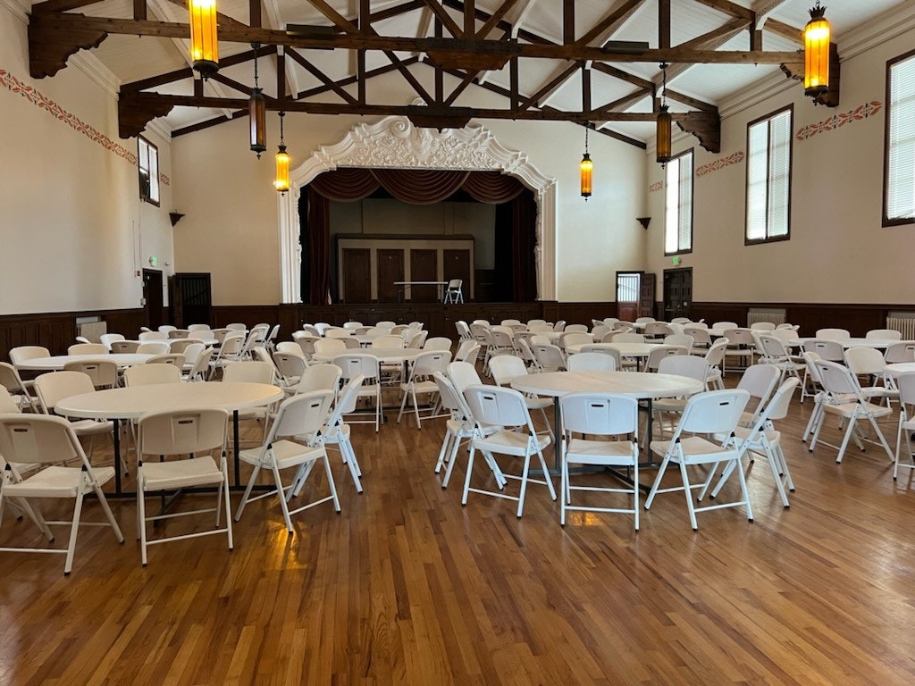 A hall with a stage, round tables, and chairs set up for an event.