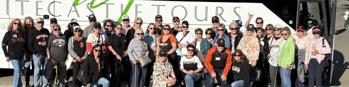 A large group of people, many wearing San Francisco Giants attire, poses in front of a tour bus.