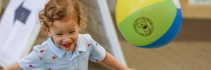 A joyful toddler playing with a colorful beach ball.