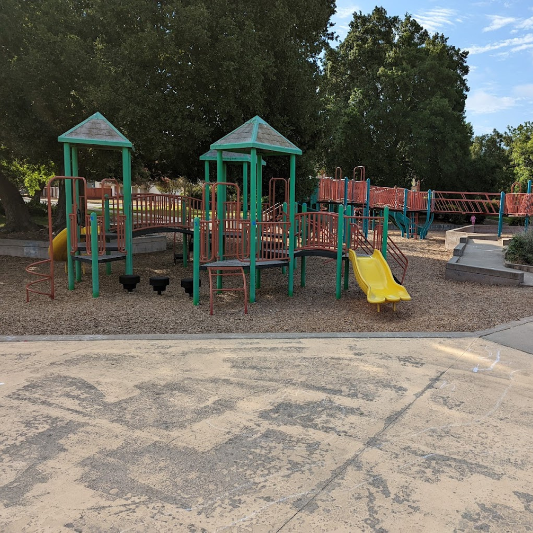 Colorful playground with slides, swings, and climbing structures, surrounded by trees.