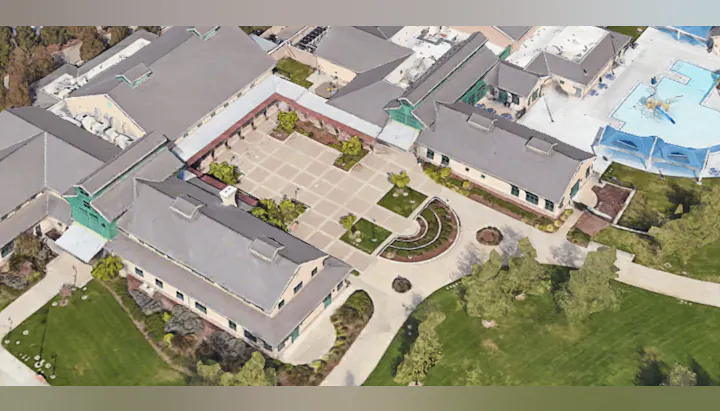 Aerial view of a large building complex with a courtyard, pathways, surrounding trees, and nearby pool.