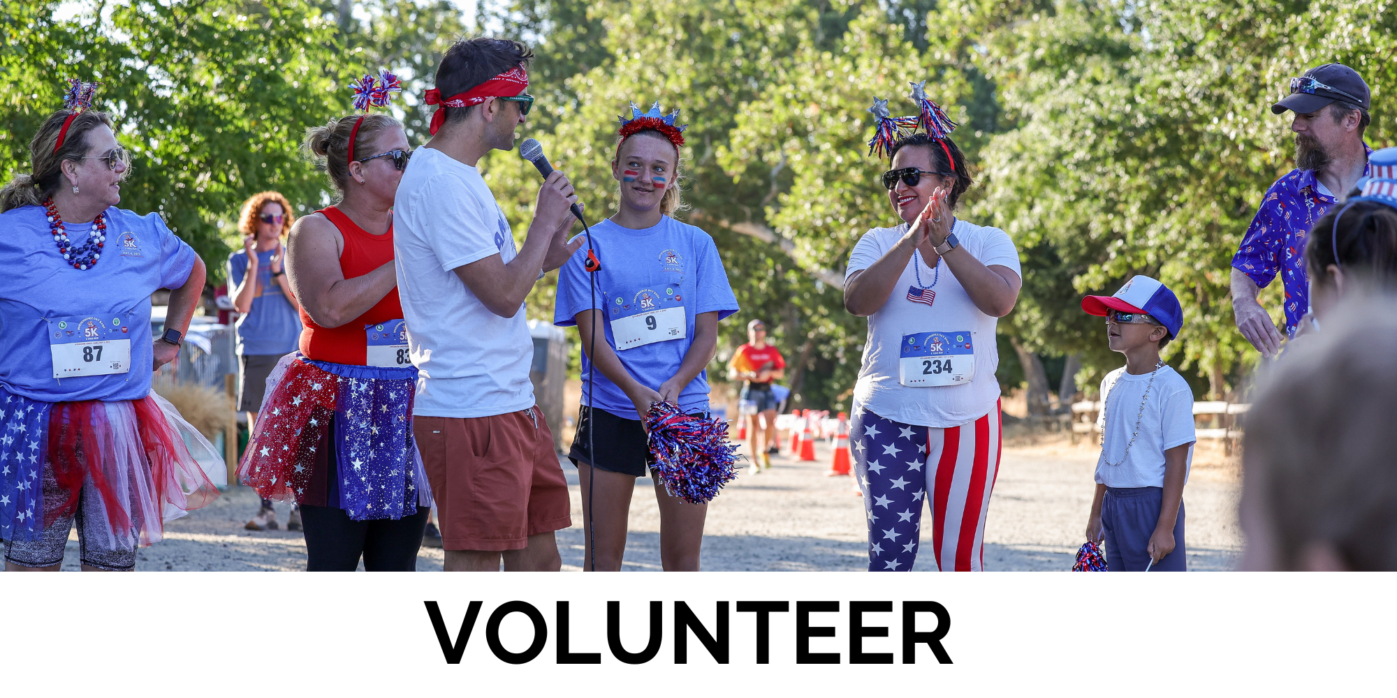 A group of volunteers is gathered, wearing festive outfits, for an event with a microphone, celebrating a fun run.