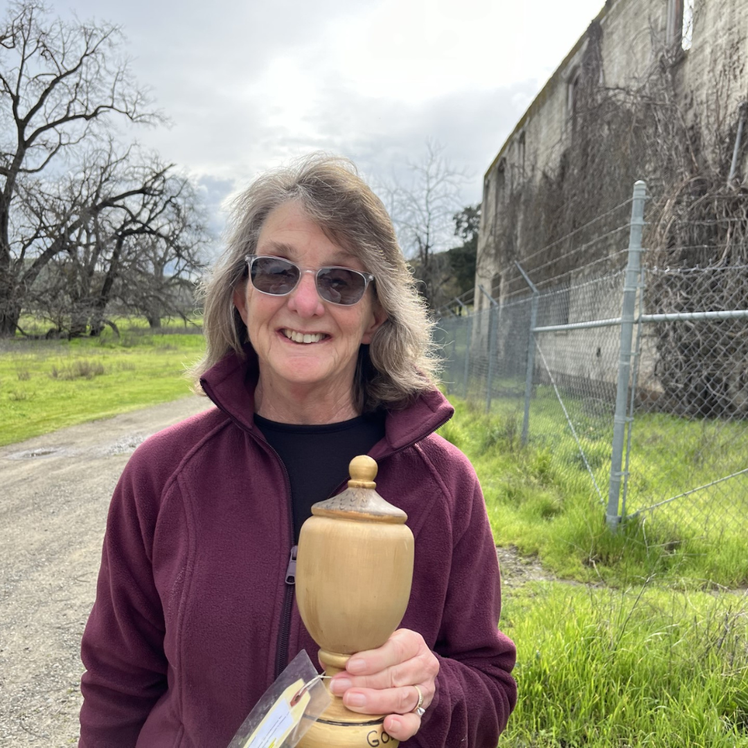 A smiling person holding a wooden trophy outdoors.