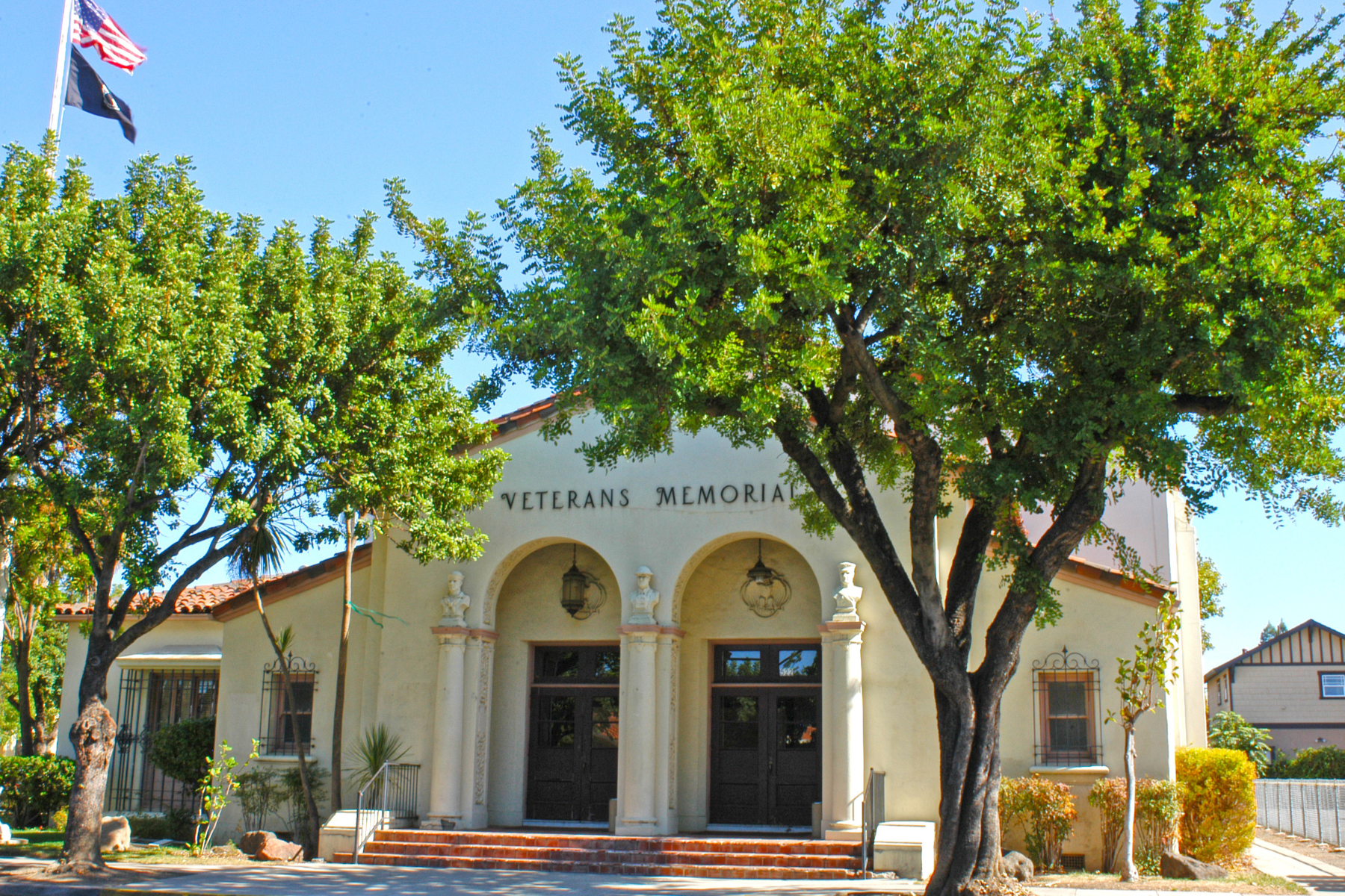 A Veterans Memorial building with an American flag, surrounded by trees under a clear blue sky.