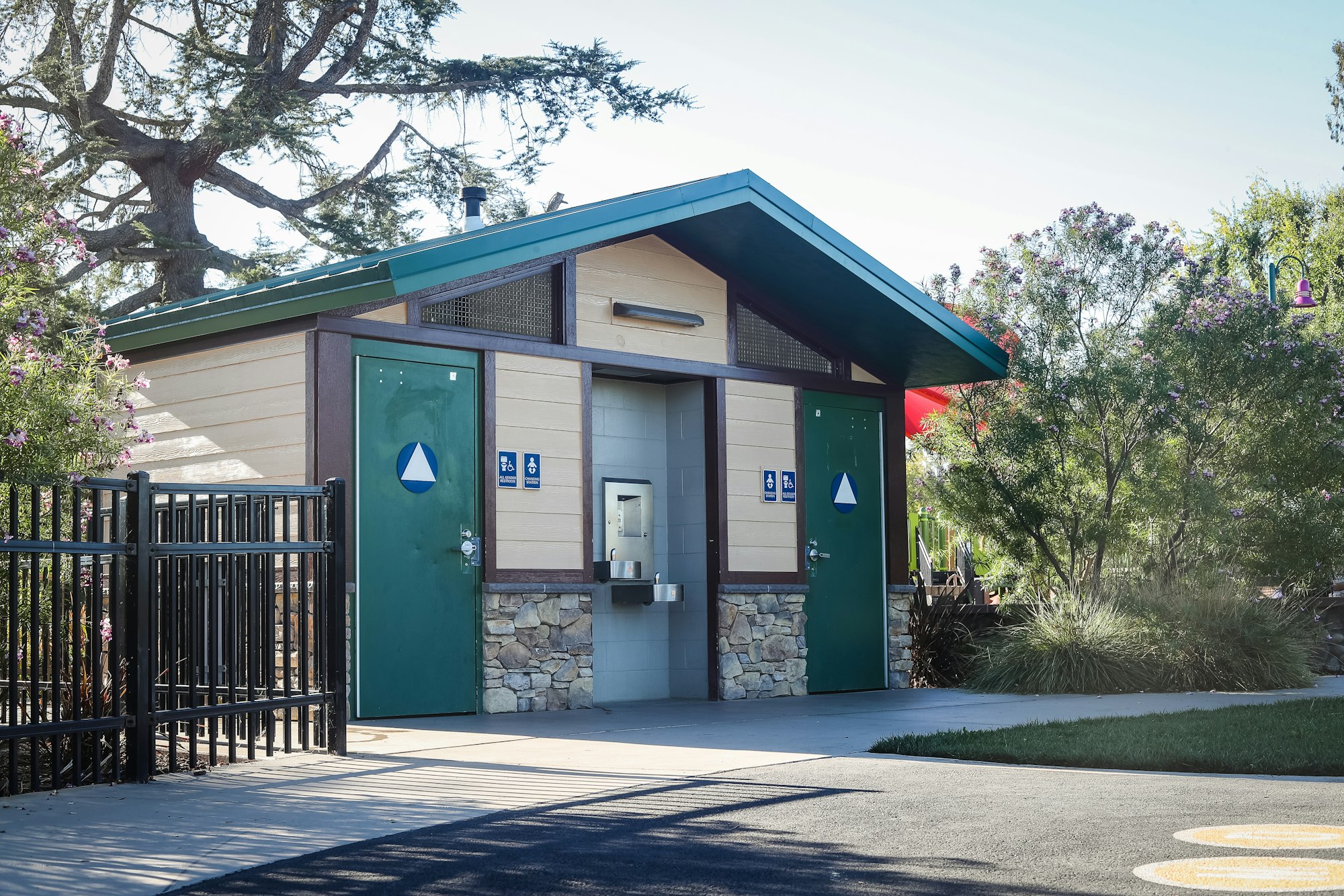 A public restroom facility with gender-neutral signage and accessibility features surrounded by greenery.