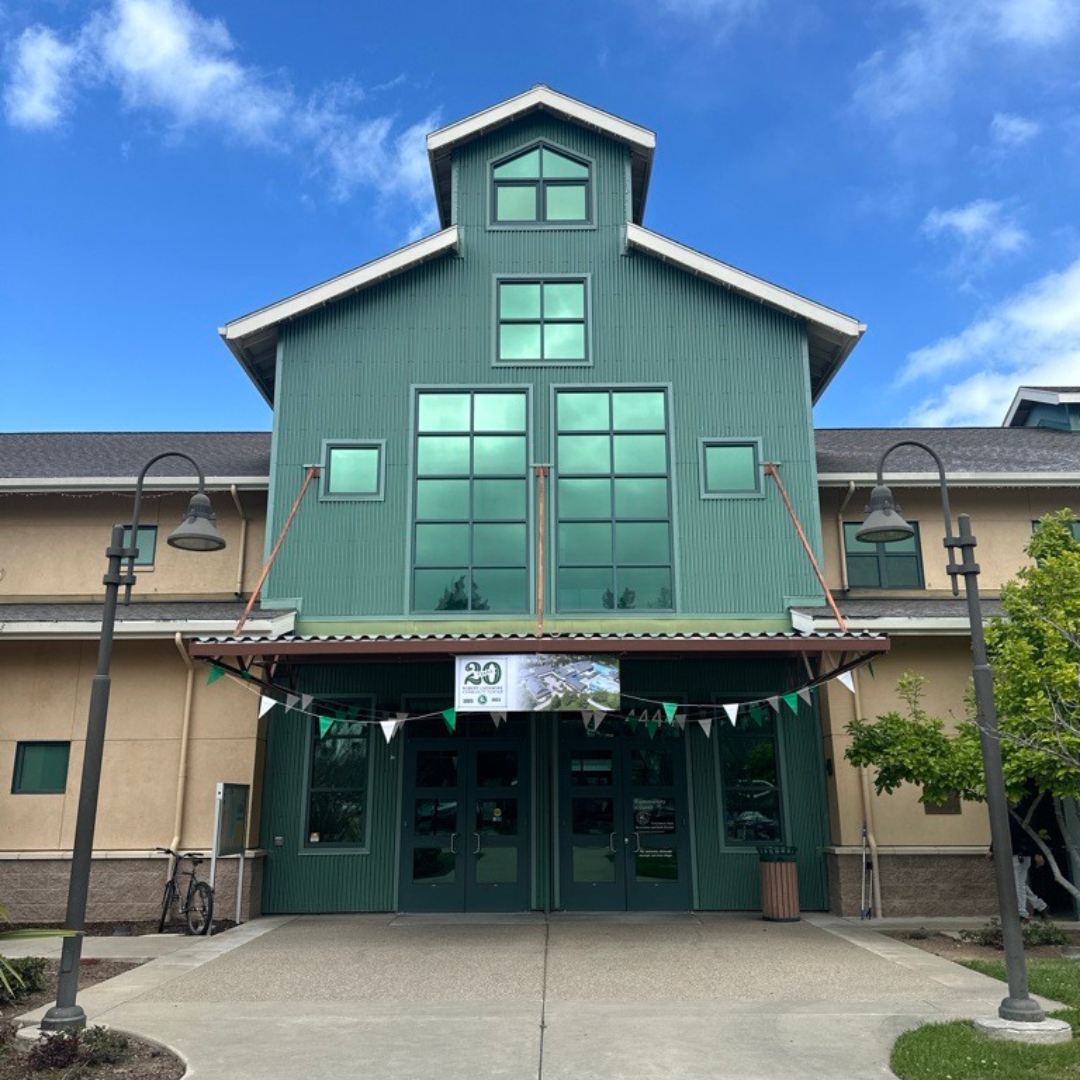 Green building with large windows, a banner, and two street lamps in front.