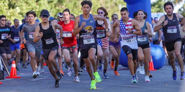 A group of runners competing in a race, some wearing colorful athletic gear, with an inflatable arch in the background.