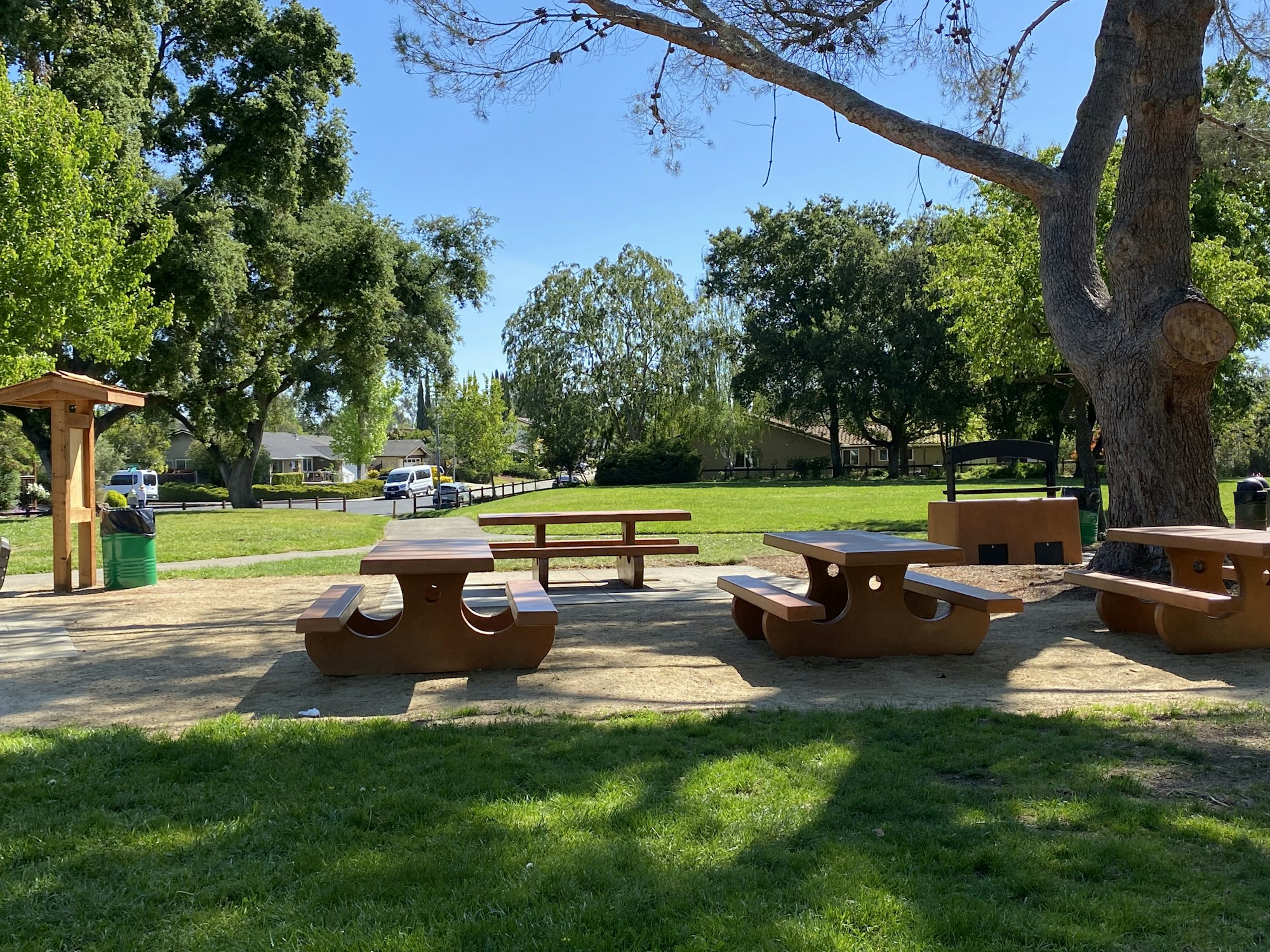 Park with benches, trees, and a trash can under a sunny sky.