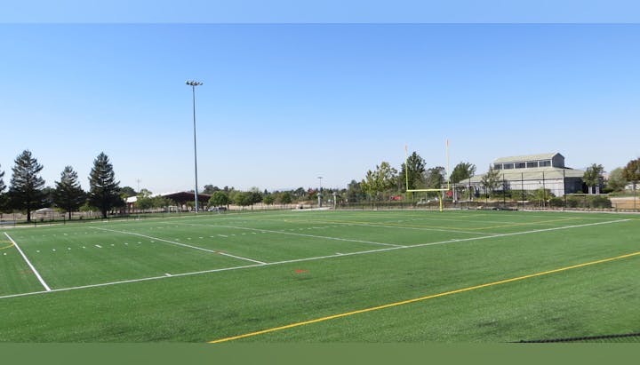 A football field with goalposts, surrounded by trees and buildings under a clear blue sky.