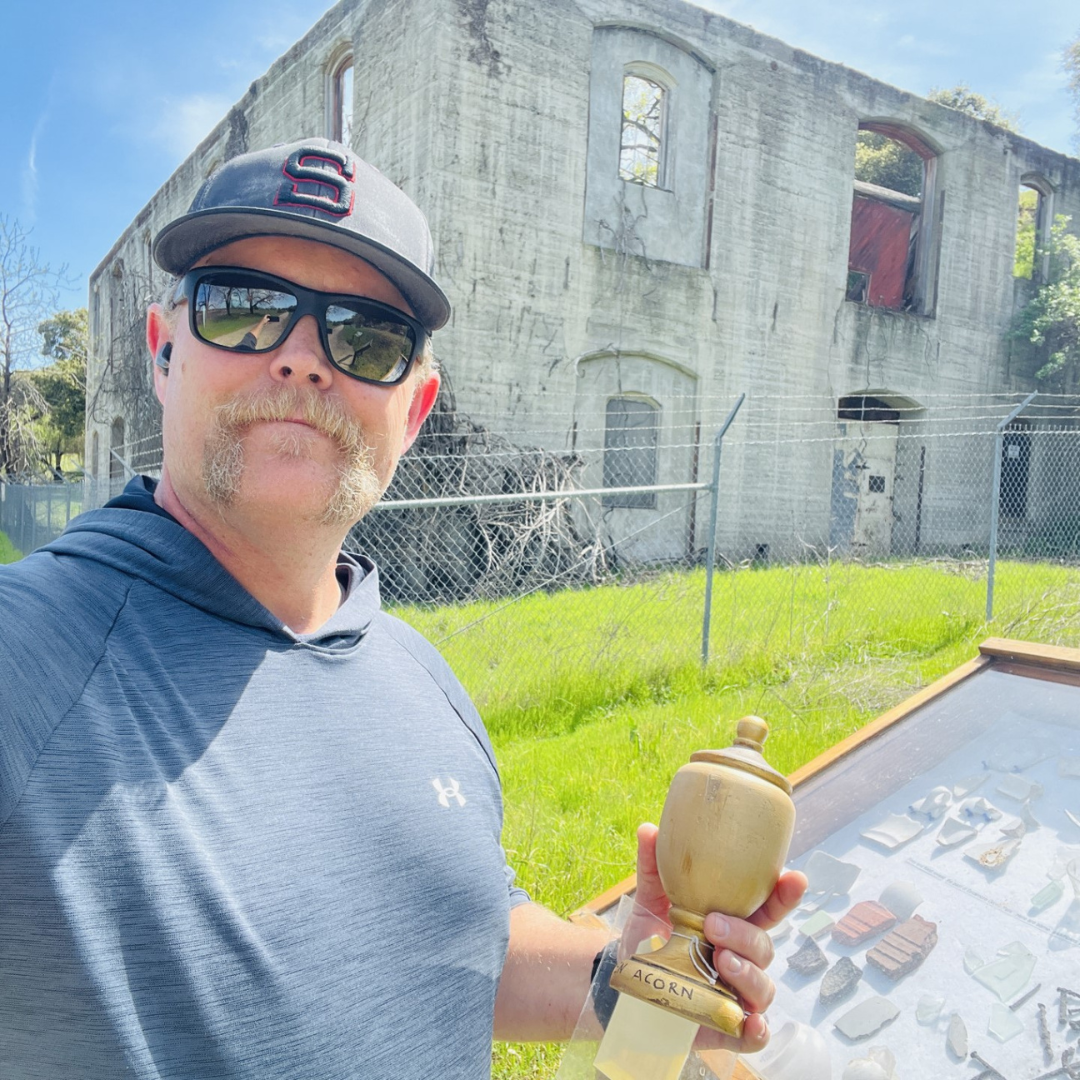 Man with an award in front of a ruined building, displaying a collection of artifacts.