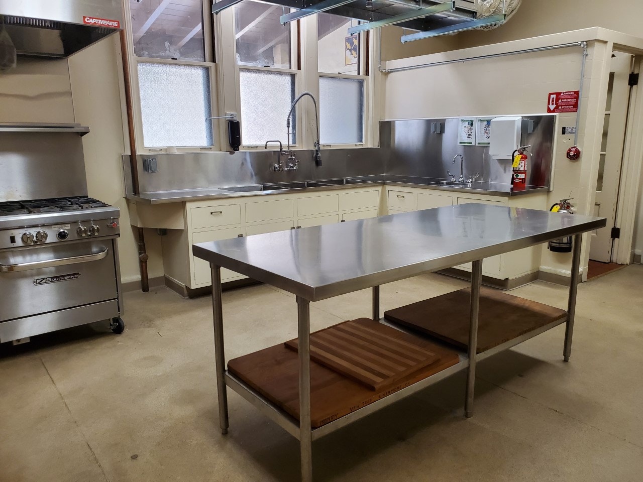 A commercial kitchen with stainless steel appliances, sinks, a large prep table, and cutting boards.