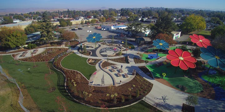 Aerial view of a colorful playground with large flower structures, seating areas, and pathways in a park setting.