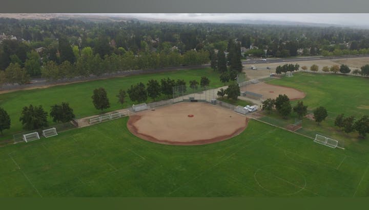 Aerial view of a park with baseball fields, soccer goals, and surrounding greenery.