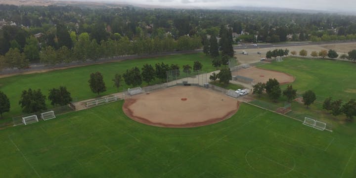 Aerial view of a park with baseball fields, soccer goals, and surrounding greenery.