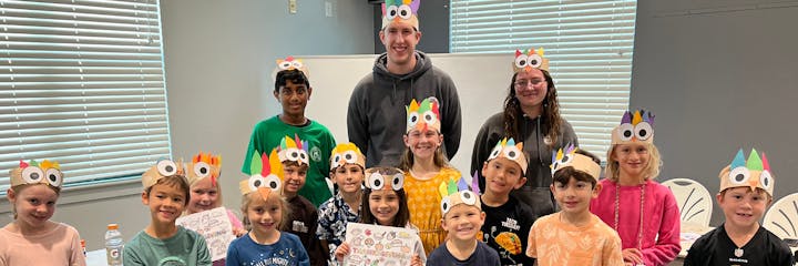 Group of smiling children wearing paper turkey hats with two adults.