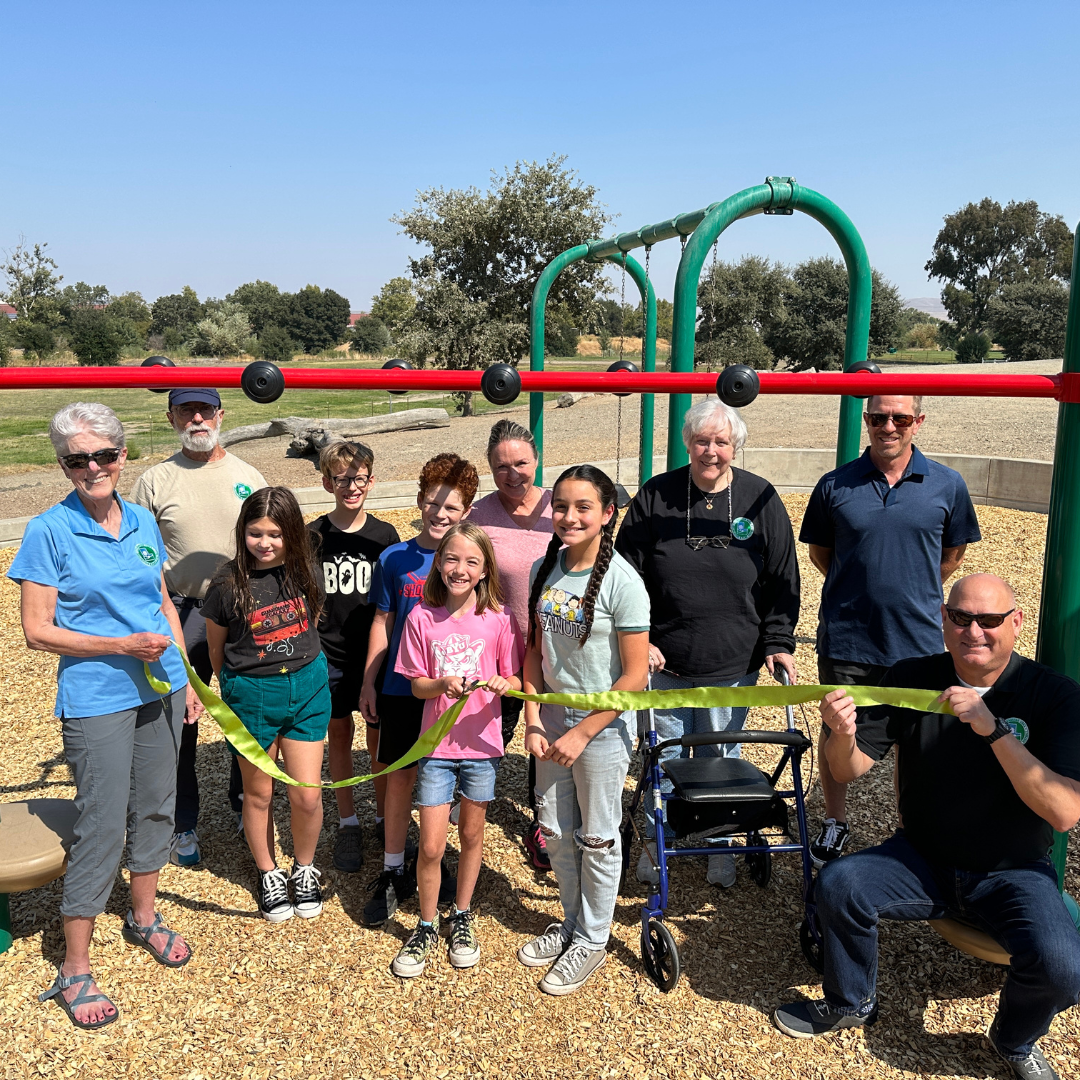 Group of people at a ribbon-cutting ceremony at a playground.