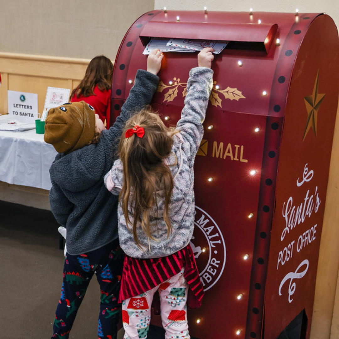 Children mailing letters at a festive "Santa's Post Office" red mailbox.