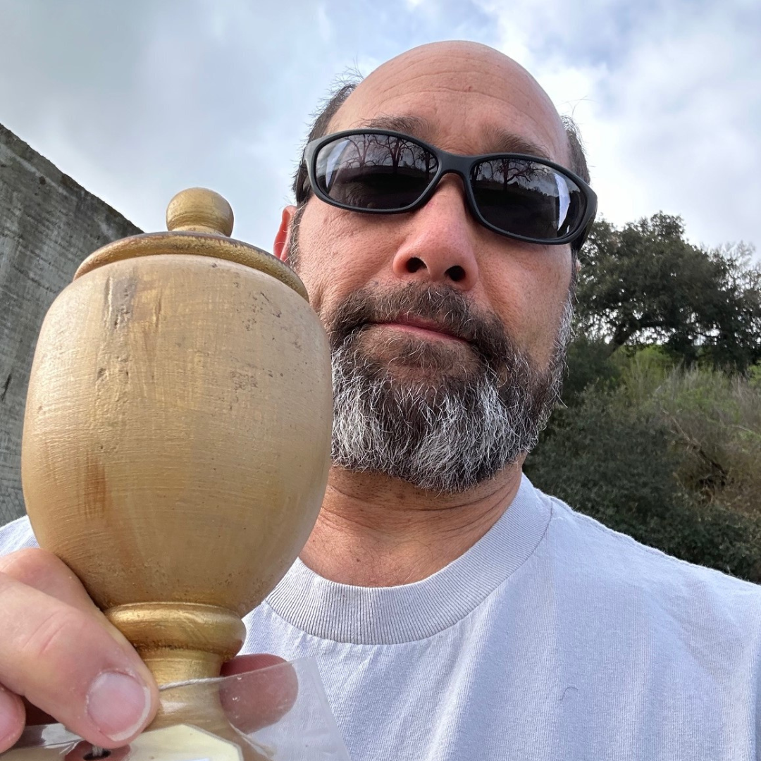 A man with sunglasses holding a wooden urn-like object outdoors.