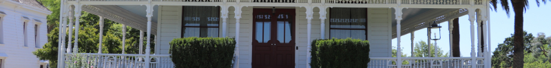 A white house with a red door, surrounded by green bushes and a porch with columns.