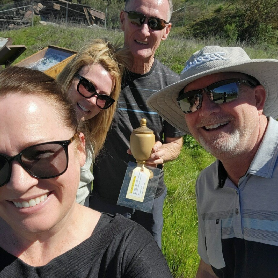 Four people smiling for a selfie outdoors, one holding a small trophy or ornament.