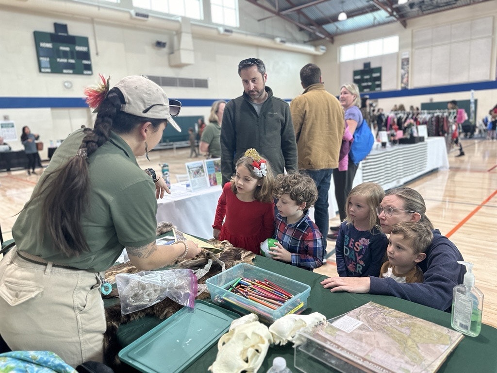 A group of children and adults engage with a presenter at an educational event, exploring nature-themed activities and exhibits.