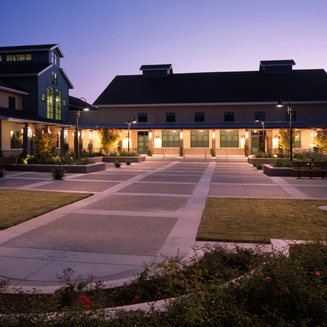 A modern building with a courtyard and landscaping, lit up at dusk.