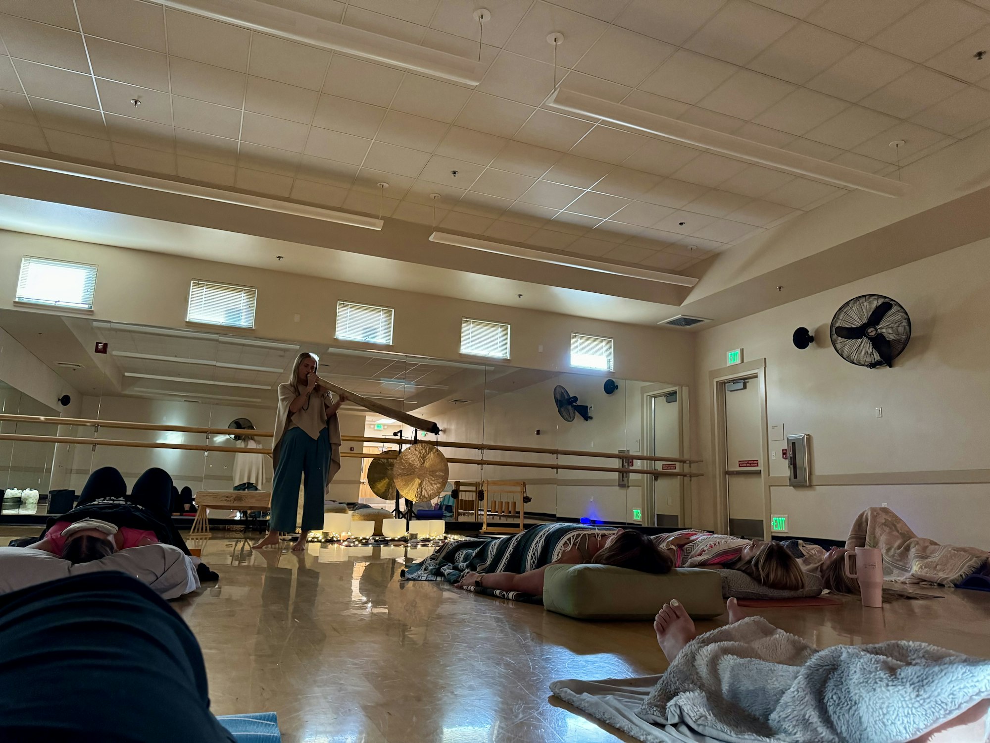 People lying on the floor in a room, covered with blankets, while someone plays a large instrument, likely for a sound meditation session.